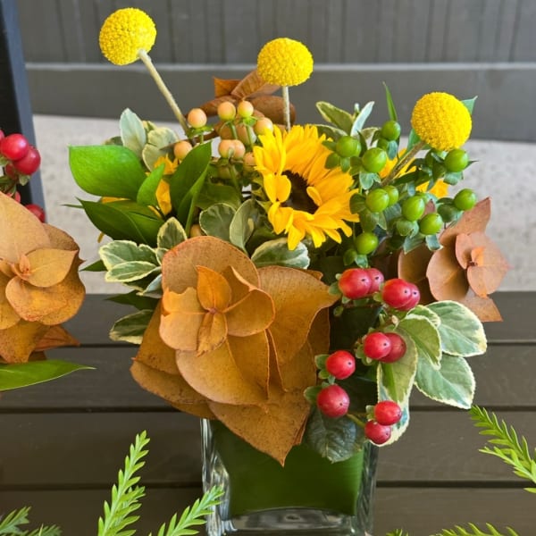 Yellow sunflower arrangement in a clear glass vase with autumn-colored accents