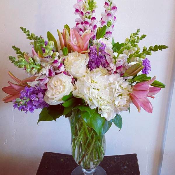 Tall bouquet of pink lilies, white roses, and purple flowers in a glass vase