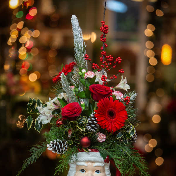 Christmas arrangement in a Santa-face mug with red flowers and pinecones