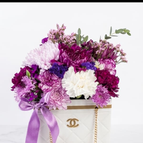 Purple and white flower arrangement in a white handbag-shaped box
