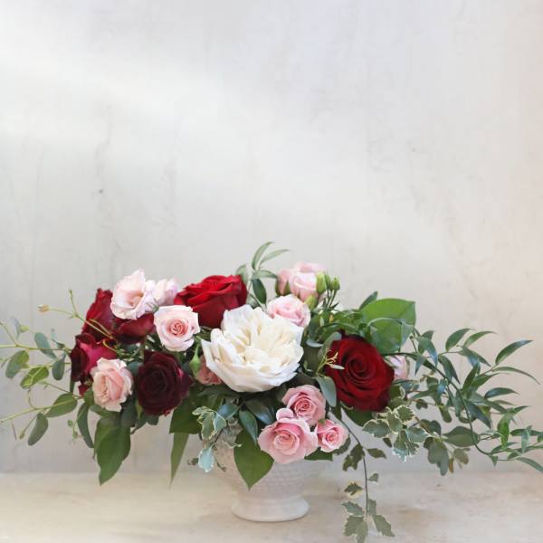 Low arrangement of red, pink, and white roses in a white vase