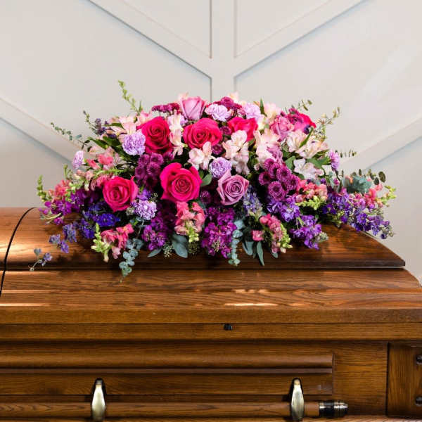 Large pink and purple floral arrangement on a wooden casket