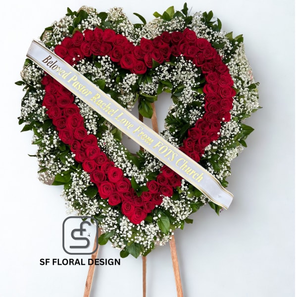 Heart-shaped standing wreath of red roses and white filler flowers with a printed ribbon across the front.