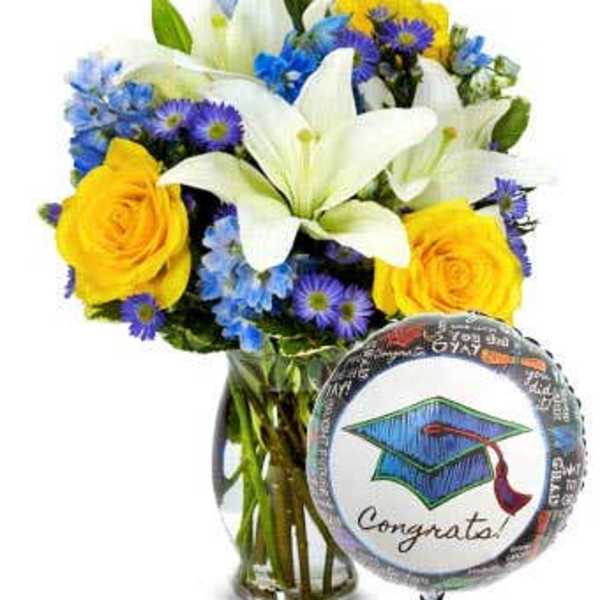 Bouquet of white lilies, yellow roses, and blue-purple flowers in a glass vase with a graduation balloon
