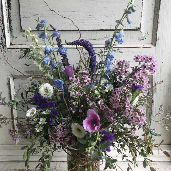 Mixed bouquet of blue, pink, and white flowers in a clear glass vase