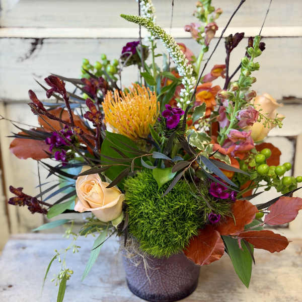 Mixed floral arrangement in a purple vase with peach and orange blooms