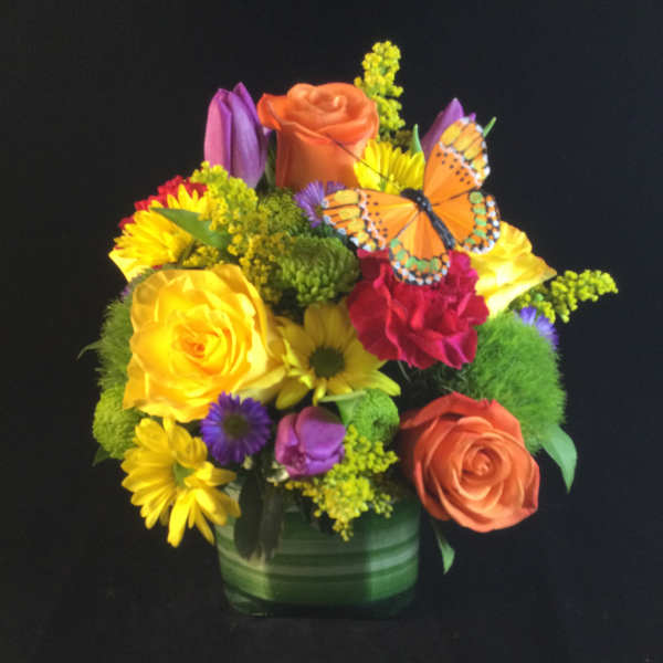 Colorful mixed bouquet in a green vase with a butterfly accent