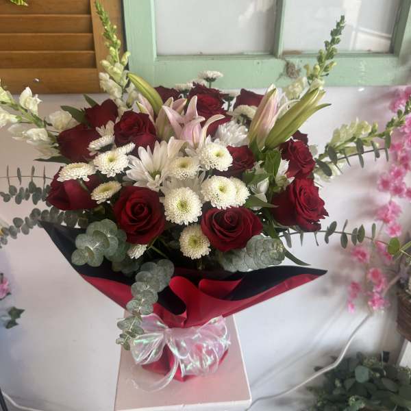Bouquet of red roses, white daisies, and pink lilies wrapped in red paper