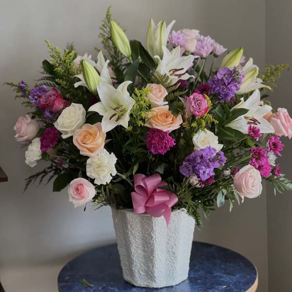 Mixed bouquet of lilies, roses, and purple flowers in a white vase