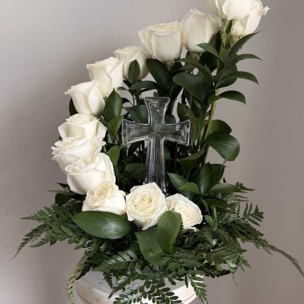 White roses arranged around a clear glass cross on a pedestal stand