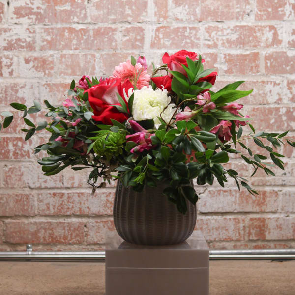 Mixed bouquet of red and pink flowers in a dark vase