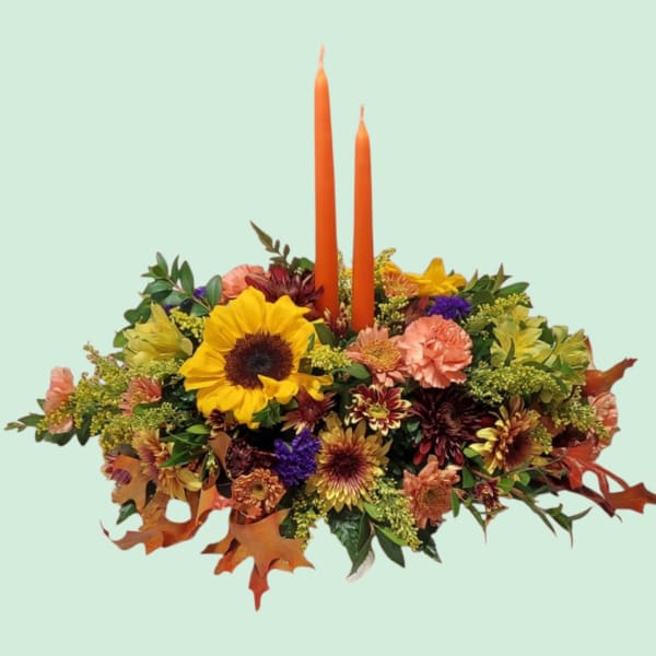 Low floral centerpiece with two orange taper candles