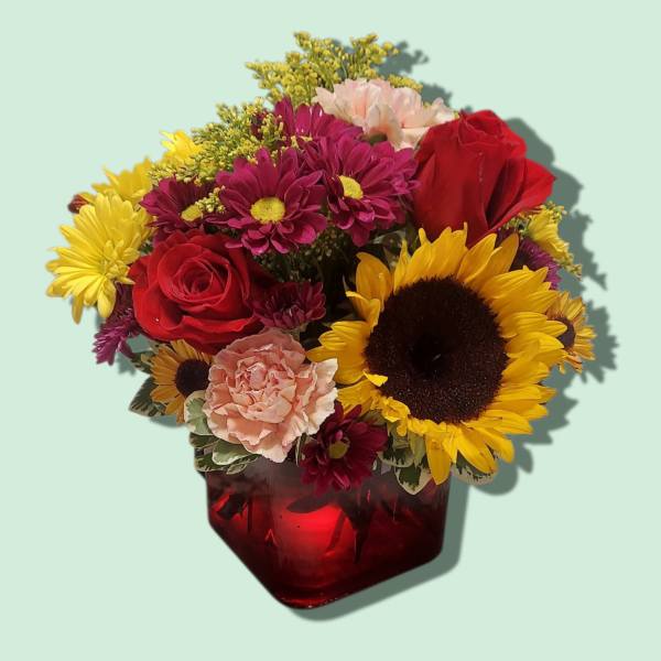 Mixed bouquet of red roses, sunflowers, and pink carnations in a red vase
