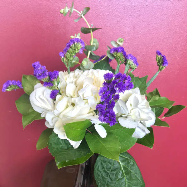 White hydrangeas and purple filler flowers in a glass vase
