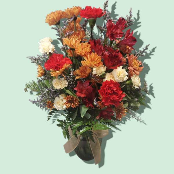 Bouquet of red, orange, and white flowers in a dark vase with a ribbon