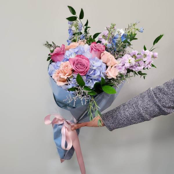 Handheld bouquet of pink roses and pastel blue flowers wrapped in blue paper