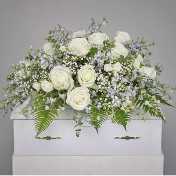 White roses and pale blue flowers arranged on a white casket