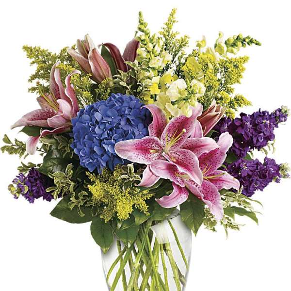 Bouquet of pink lilies, blue hydrangea, and purple flowers in a glass vase