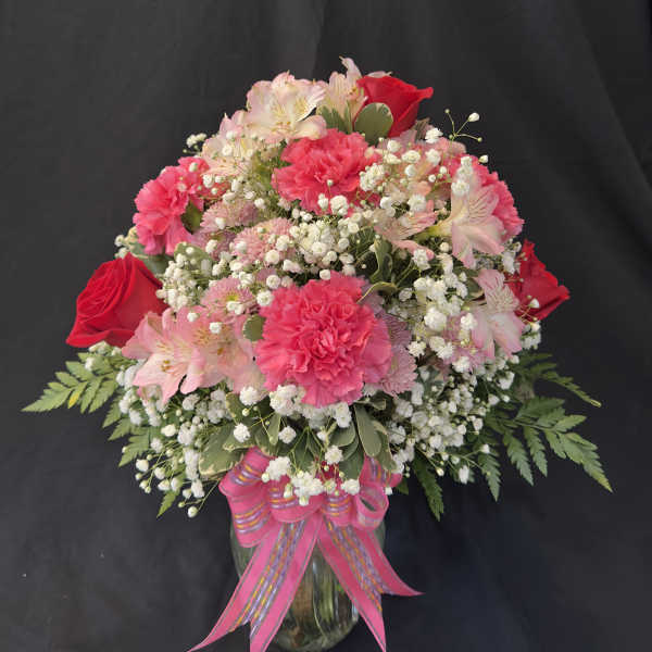 Pink and red flower arrangement in a glass vase with a pink ribbon