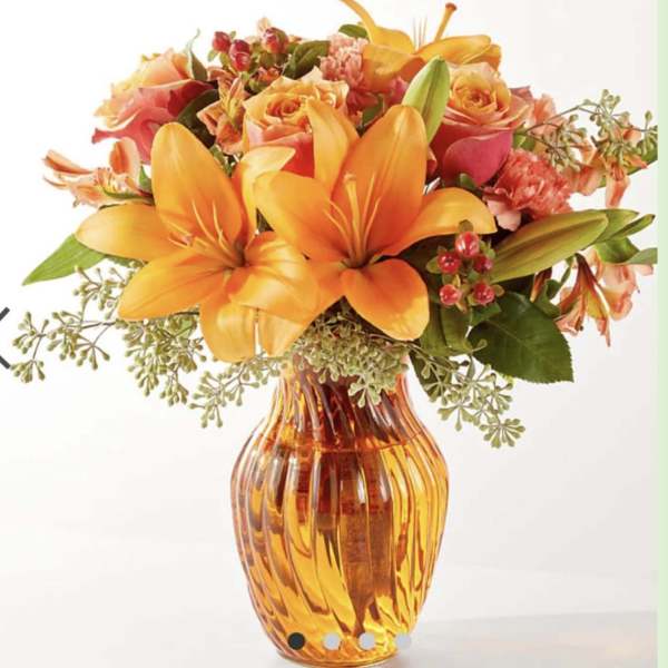 Orange lilies and peach roses arranged in an amber glass vase