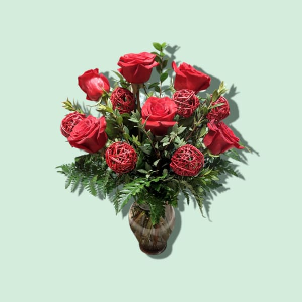 Red roses arranged in a glass vase with decorative red spheres