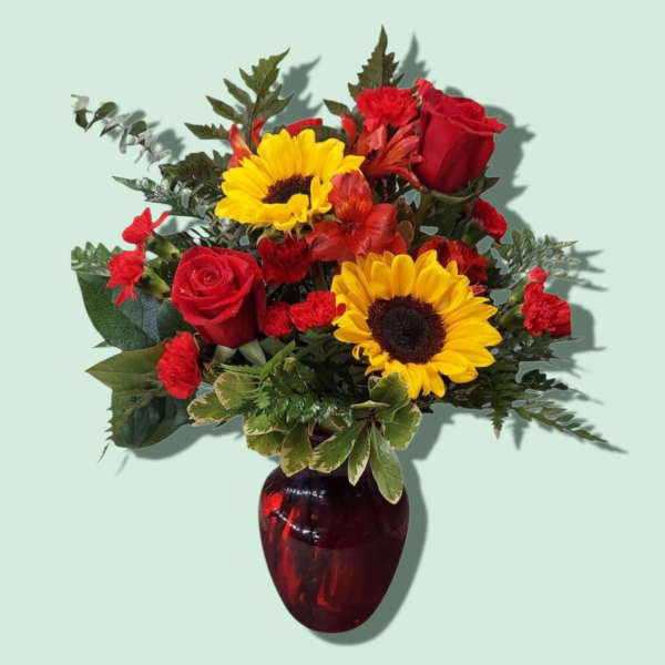 Bouquet of red roses and yellow sunflowers in a red glass vase