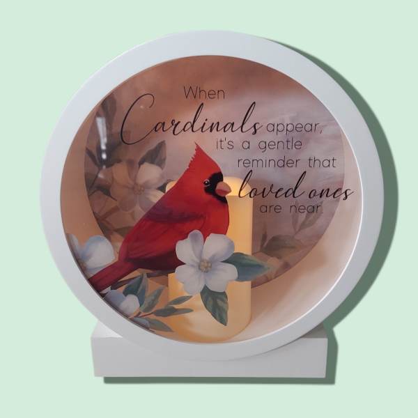 Round memorial plaque with a red cardinal, flowers, and a candle