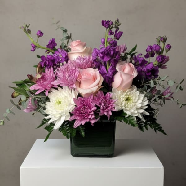 Pink roses and purple chrysanthemums arranged in a square glass vase