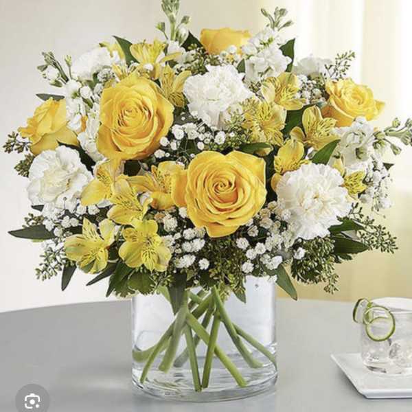 Yellow roses and white flowers arranged in a clear glass vase