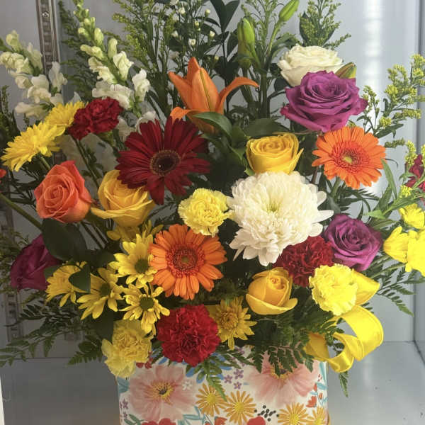 Colorful mixed flower arrangement in a floral-print box with a yellow ribbon