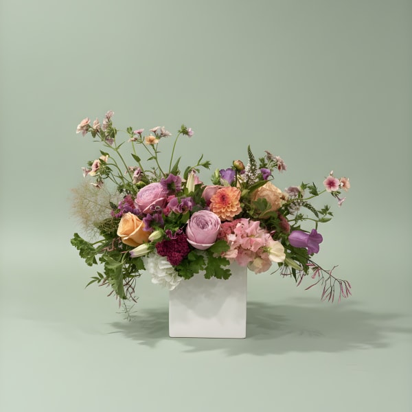 Mixed pink, peach, and purple flowers in a white vase
