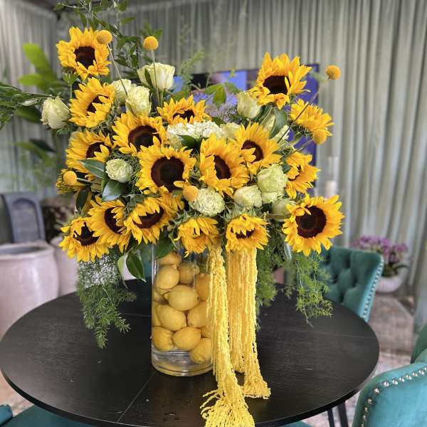 Sunflower arrangement in a clear vase with lemons and trailing yellow flowers