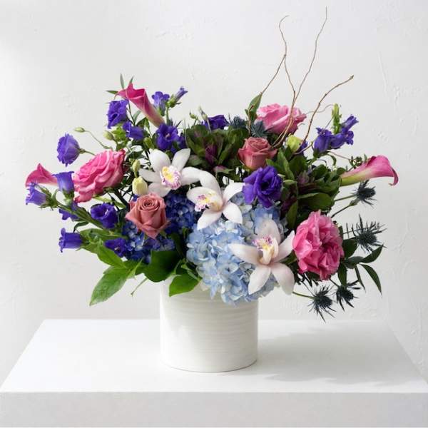 Mixed bouquet of pink, purple, and white flowers in a white vase
