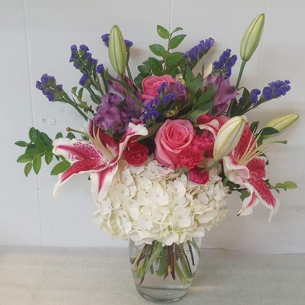 Mixed bouquet of pink roses, lilies, and white hydrangea in a glass vase