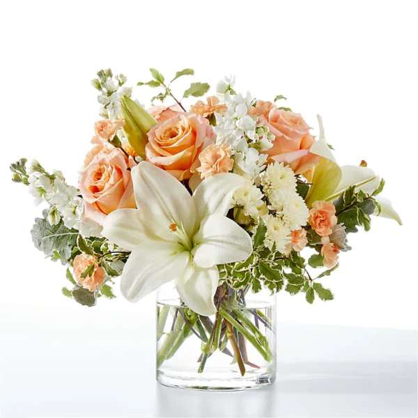 Peach roses and white lilies arranged in a clear glass vase