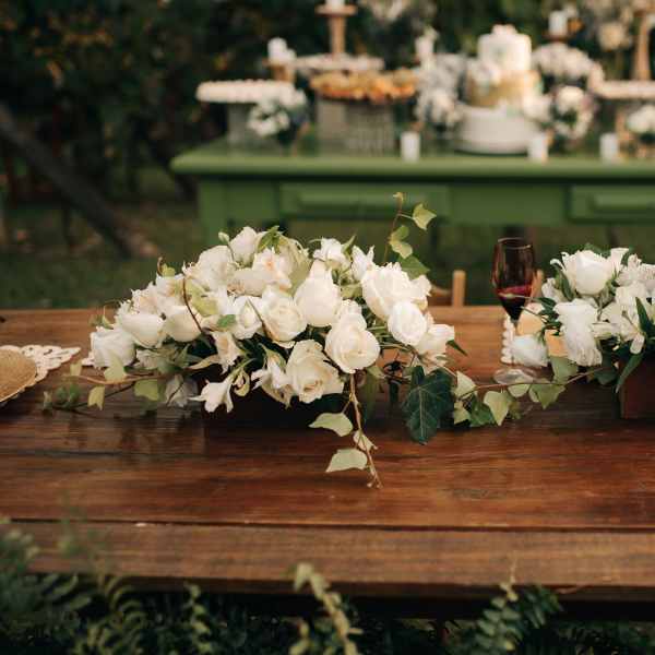 Two white floral centerpieces on a wooden table with wine glasses