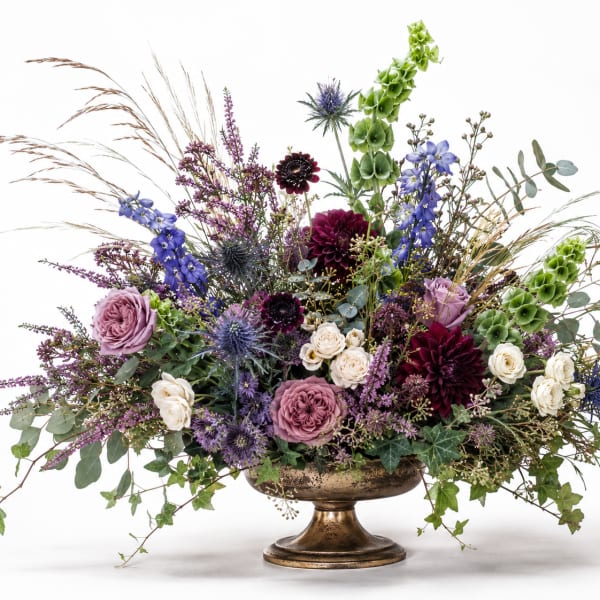 Mixed floral arrangement in a gold pedestal vase with purple, white, and green blooms