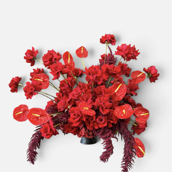 Red floral arrangement with roses and anthuriums in a dark vase