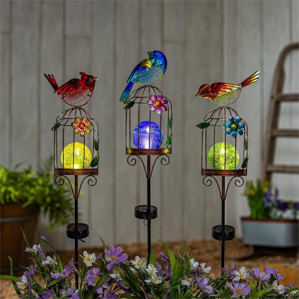 Three colorful bird garden stakes with glowing orb lights above purple flowers