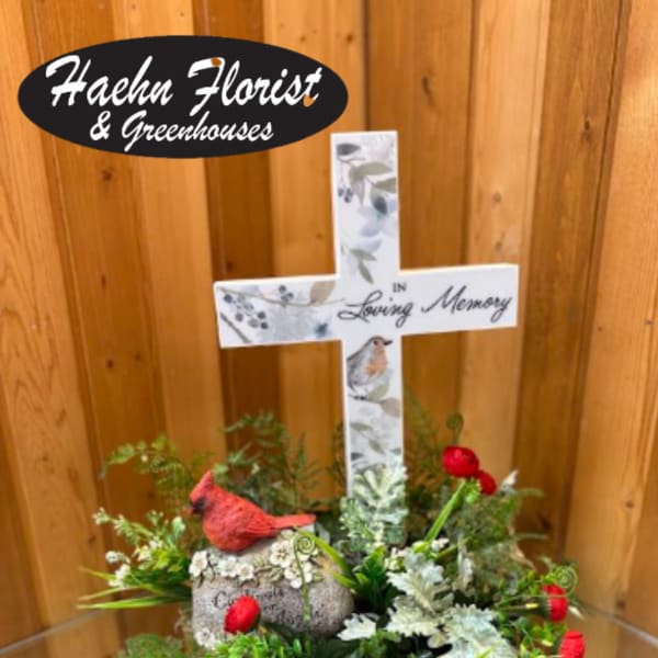 Memorial cross arrangement with red flowers and a bird figurine