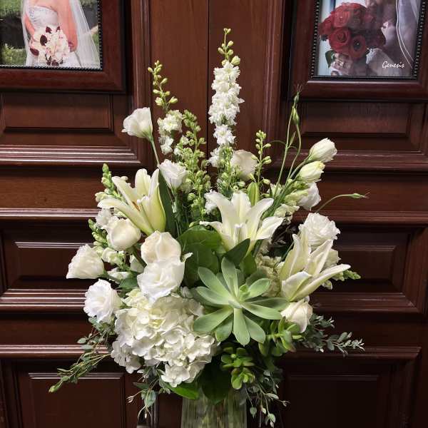 White floral arrangement in a clear glass vase with lilies and hydrangeas