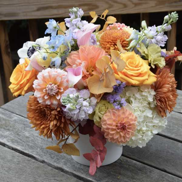 Mixed bouquet of orange, pink, white, and lavender flowers in a white vase