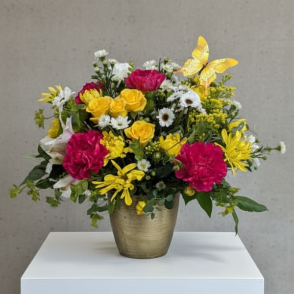 Bright mixed flower arrangement in a gold vase with a yellow butterfly accent.