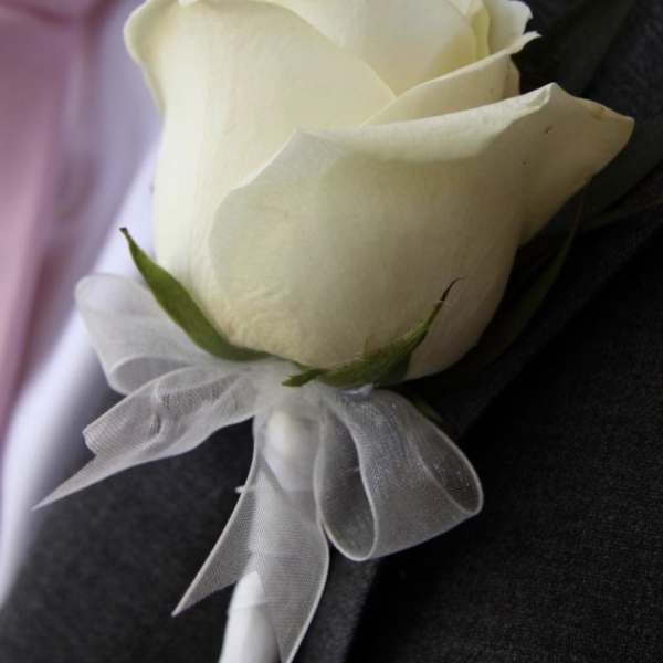 White rose boutonniere with a sheer ribbon on a dark suit lapel