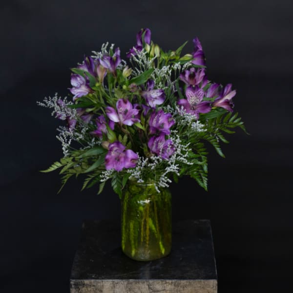 Purple alstroemeria bouquet in a green glass jar vase