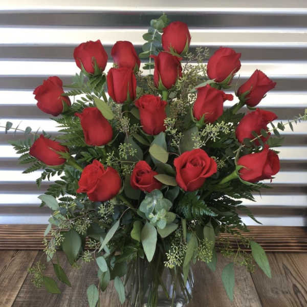 Red roses arranged in a clear glass vase with greenery