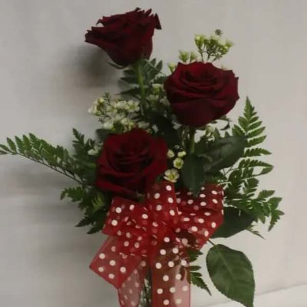 Three red roses in a glass vase with a red polka-dot bow
