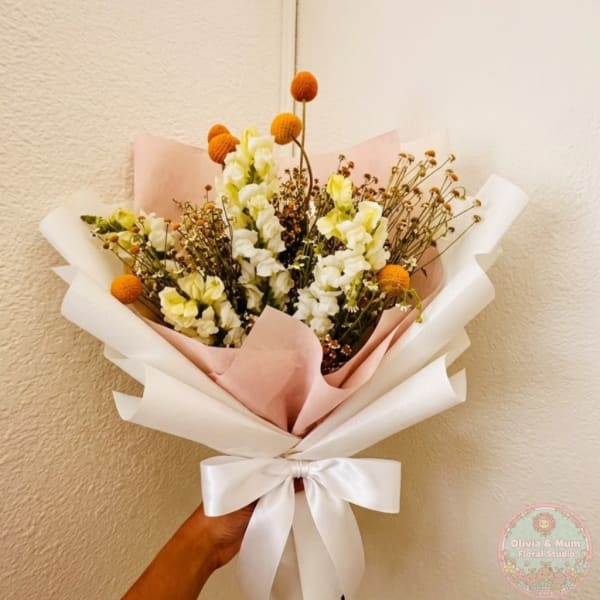 Handheld bouquet of white and pale yellow flowers wrapped in pink and white paper