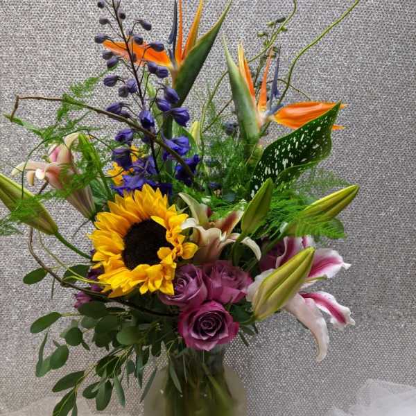 Mixed bouquet with sunflowers, roses, lilies, and bird of paradise in a vase