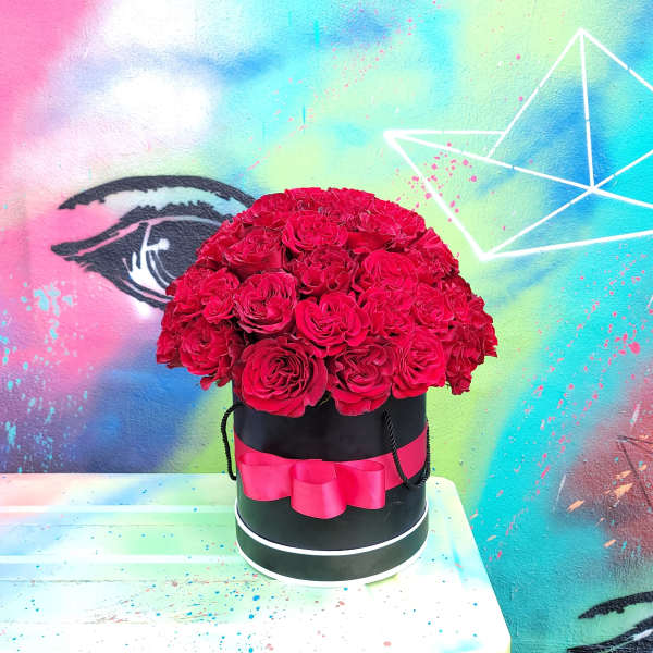 Red roses arranged in a black round box with a pink ribbon